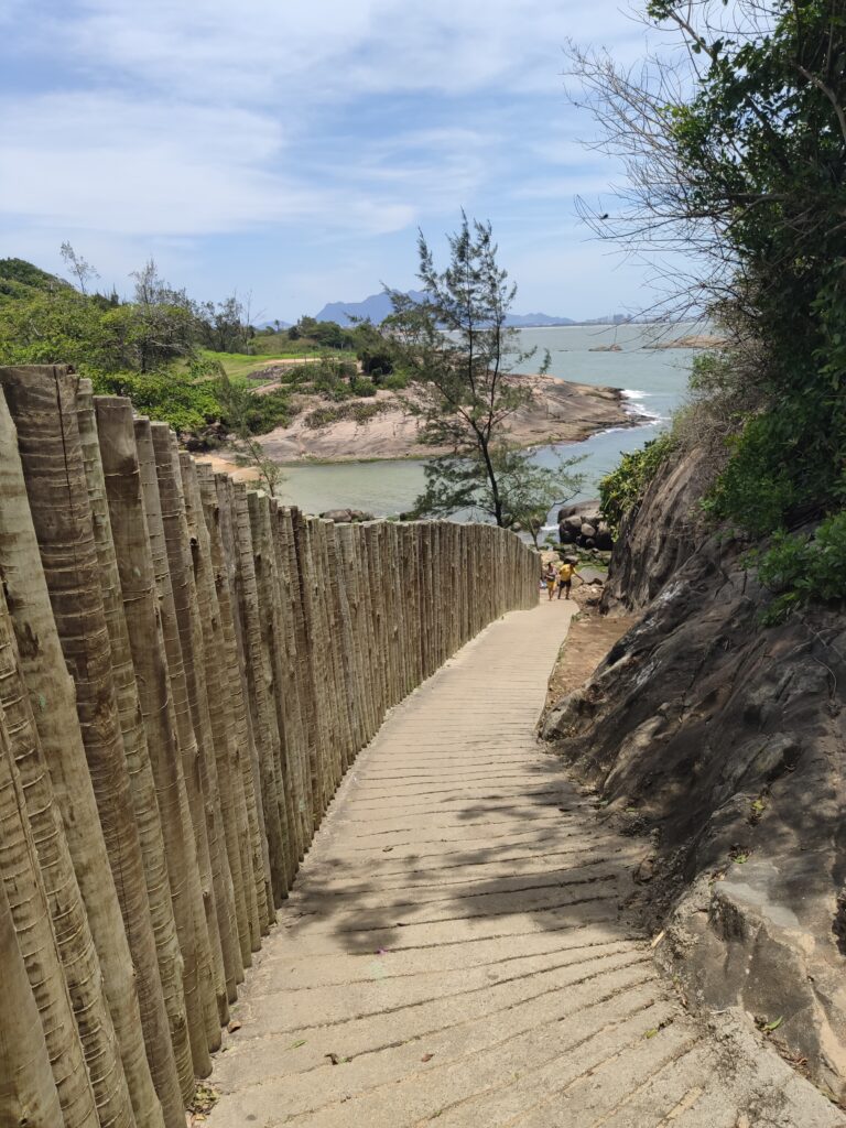 Imagem mostrando um caminho cercando por muro de madeira e que leva a uma praia escondida