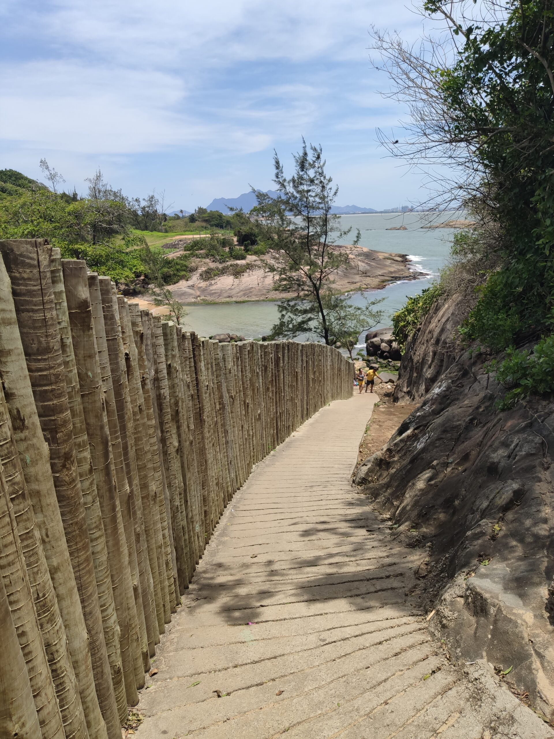 Imagem mostrando um caminho cercando por muro de madeira e que leva a uma praia escondida